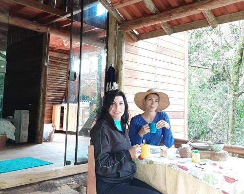 AnnitapolisCabanas Pousada Esmeraldas的两个女人坐在桌子边喝杯咖啡