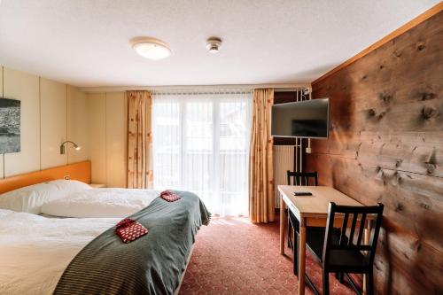 萨斯费Hotel Les Amis的酒店客房配有一张床、一张书桌和一台电视。