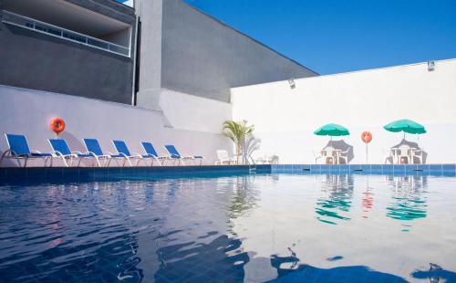 伊瓜苏Hotel Dan Inn Express Foz do Iguaçu的一座带椅子和遮阳伞的游泳池位于一座建筑旁边