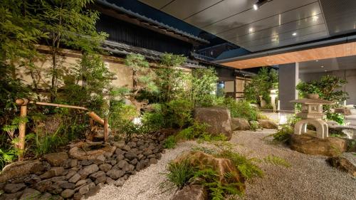 京都HOTEL UNIZO Kyoto Karasuma Oike的一座建筑中种有岩石和树木的花园