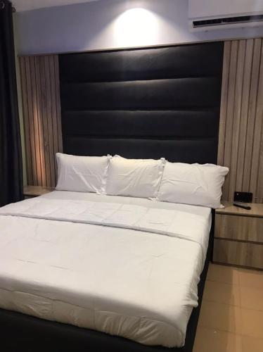 哈科特港QARAS HOUSE 3 HOTELS的一张带黑色床头板、白色床单和枕头的床