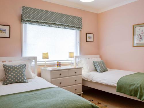 EdzellThe Butchers Cottage的一间卧室设有两张床、一个窗口和一个梳妆台。