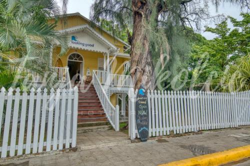 南圣胡安Looking Good Surf House San Juan del Sur的黄色的房子,有白色的栅栏和一棵树