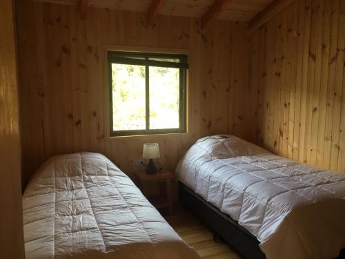 Los QueñesLos Quenes River Lodge的小木屋内的两张床,设有窗户