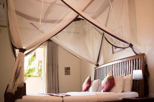 恩德培Entebbe Palm Hotel的卧室配有带枕头的天蓬床和窗户。