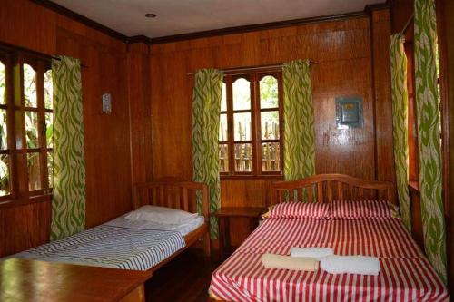 圣维森特Nellie's Tourist Inn- Port Barton的配有木墙和窗户的客房内的两张床