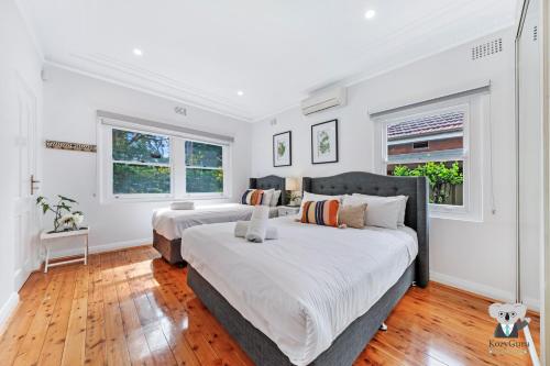 悉尼KozyGuru / Rockdale / Spacious Modern 2 Bedrooms Holiday Home NRO147的卧室设有两张床,拥有白色的墙壁和木地板