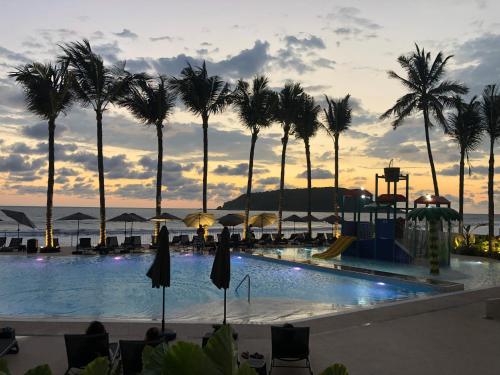 马萨特兰Viaggio Resort Mazatlán的棕榈树泳池和日落背景