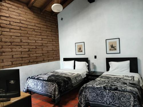 萨卡特兰Cabañas y habitaciones Los Cedros的一间卧室设有两张床、一台电视和砖墙