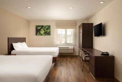 梅里达Extended Suites Merida Siglo XXI的酒店客房设有两张床、一张桌子和一台电视。