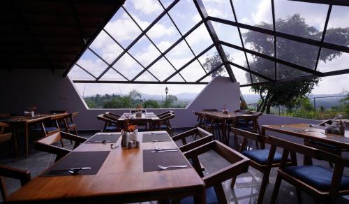 RāmanagaramRavishing Retreat Resort的餐厅设有木桌、椅子和大窗户。