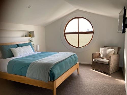 坎贝尔港12 Rocks Beach View Loft Central Port Campbell的一间卧室设有一张床、一个窗口和一把椅子