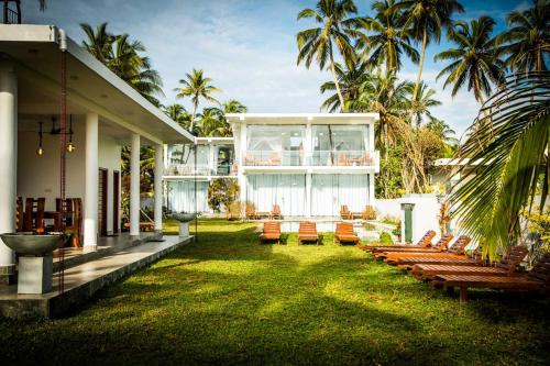 Paiyagala SouthInfinity of Sri Lanka的一座带草坪的房屋,草坪上摆放着椅子和棕榈树