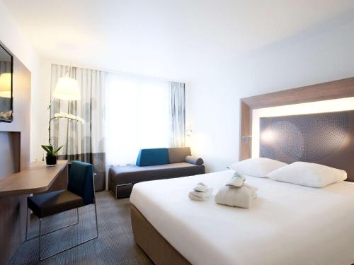 巴塞尔巴塞尔市诺富特酒店的酒店客房设有一张白色大床和椅子