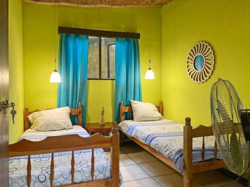 奥罗西Montaña Linda Hostel Orosi的配有两张床铺的客房,拥有绿色的墙壁和蓝色的窗帘
