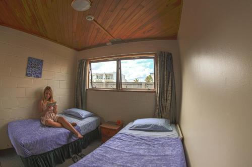 派西亚Centabay Lodge and Backpackers的坐在床边的两床间里的一个女人