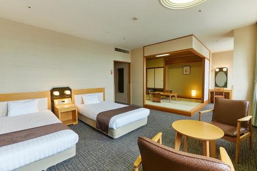 一关KAMENOI HOTEL Ichinoseki的酒店客房带两张床和一张桌子以及椅子。