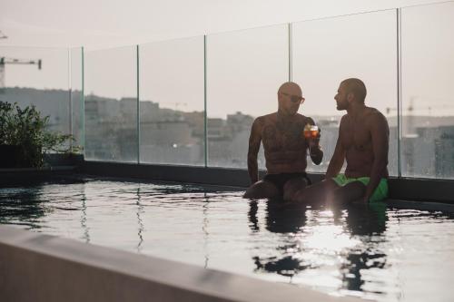 圣保罗湾城ibis Styles ST Pauls Bay Malta的两个男人坐在游泳池的水里
