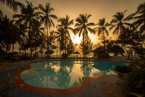 乌罗阿F-Zeen Boutique Hotel Zanzibar的日落前种有棕榈树的游泳池