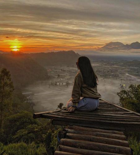 Baturajapinggan sunrise glamping的坐在山顶上看日出的女人