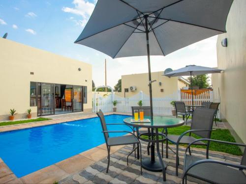 卢萨卡Pebble View Luxury Apartments的游泳池旁配有遮阳伞的桌椅
