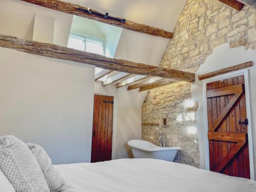 奇平卡姆登Grooms Lodge, Chipping Campden - Taswell Retreats的一间卧室设有石墙、一张床和一个水槽