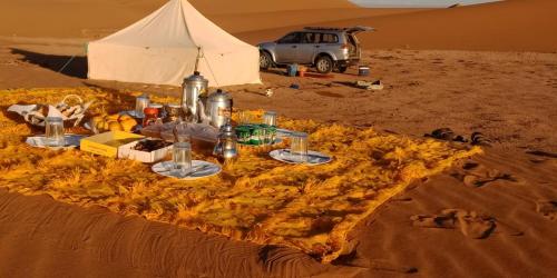 扎古拉Tikida Camp by tinfou的沙漠中一张桌子,上面有帐篷