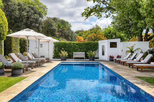 开普敦Villa Coloniale Schumacher Luxury Retreat的庭院旁的游泳池配有椅子和遮阳伞