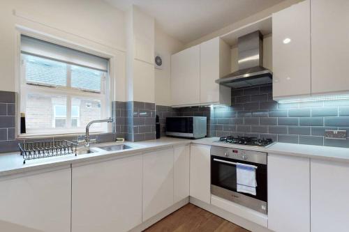 伦敦Lovely 2-bedroom flat with parking near Highgate的厨房配有白色橱柜、水槽和炉灶。