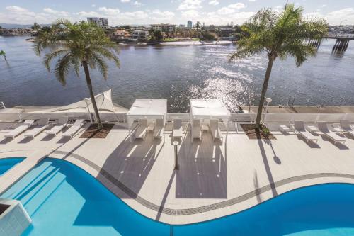 黄金海岸黄金海岸韦伯酒店的水边的游泳池,设有椅子和棕榈树