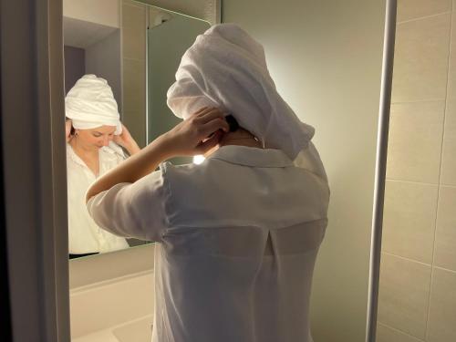Ars-LaquenexyB&B HOTEL Metz Est Technopole Pôle Santé的穿白色长袍的女人,看着镜子