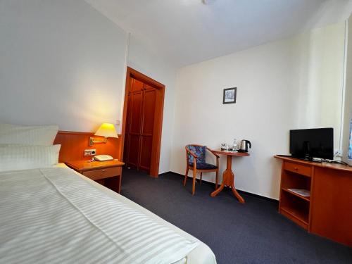 诺伊基兴Hotel Zur Stadt Cassel的酒店客房配有一张床和一张书桌及一台电视