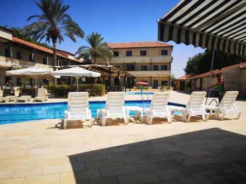杰里科巴巴尔沙姆度假酒店的一组白色的椅子和桌子,旁边是游泳池