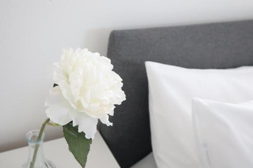 伦敦Twelve Thirty Serviced Apartments - Balham的睡床旁边的花瓶里白色的花