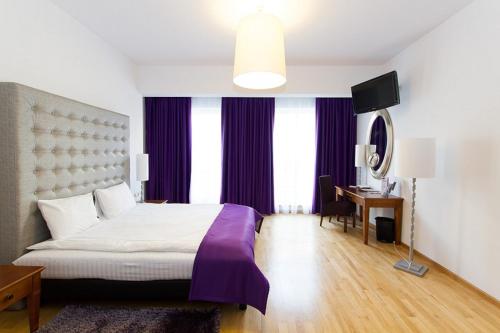 波兹南丹普雷斯提齐酒店的一间卧室配有一张大床、紫色窗帘和一张书桌