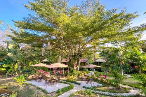 库德岛Baan Bua Cottage SHA EXTRA PLUS B5510的花园设有桌子、遮阳伞和树木