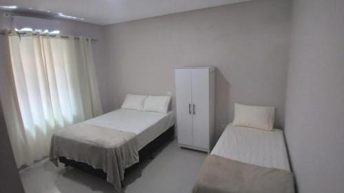 伊瓜苏Casa aconchegante com piscina e bem localizada的白色的客房设有两张床和橱柜。