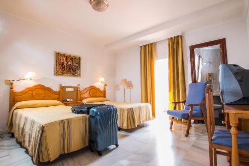 洛哈Hotel Abades Loja的酒店客房,配有一张带行李箱和书桌的床