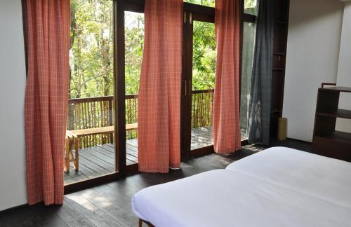 瓦亚纳德Uravu Bamboo Grove Resort的一间卧室设有一张床,阳台设有滑动玻璃门