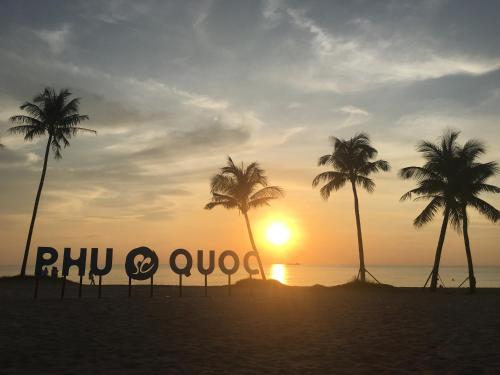 富国Minh Anh Hotel的棕榈树海滩上的标志和日落