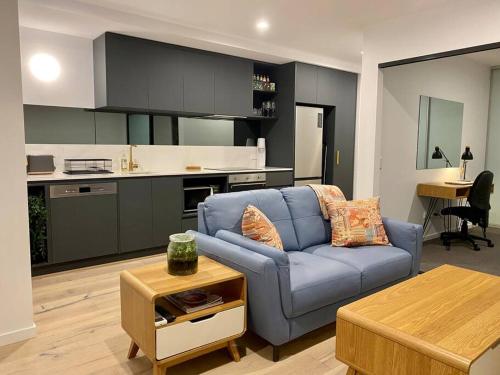 堪培拉Central Canberra City apartment with study and full amenities including parking的一间带蓝色沙发的客厅和一间厨房