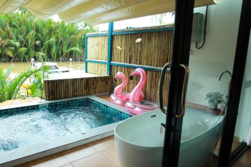 素叻Phetrapoolvilla (เภตราพูลวิลล่า)的带浴缸的浴室以及带粉红色火烈鸟的游泳池。
