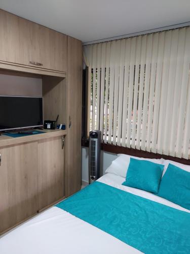 麦德林Apartaestudio Laureles - Viva Laureles的一间卧室配有一张带蓝色枕头的床和电视。