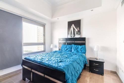 圣多明各Luxurious 2BDR condo located in Prestigious Tower.的一间卧室配有一张带蓝色棉被的床和窗户。