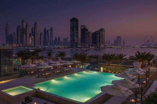 迪拜Radisson Beach Resort Palm Jumeirah的一个带遮阳伞的游泳池,晚上则享有城市天际线