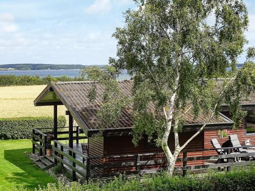 斯文堡8 person holiday home in Svendborg的小屋前面有树和椅子