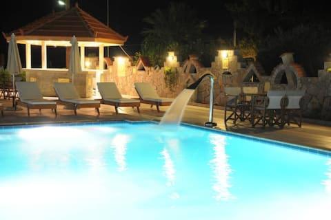 赫索尼索斯Evalia Apartments的一个带椅子的游泳池,晚上还有喷泉