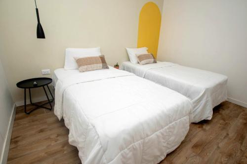 QuesadaHotel Ventura的客房设有两张带白色床单和桌子的床。