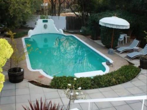 布隆方丹La Belle Guest House的庭院内的游泳池,配有两把椅子和一把遮阳伞