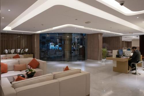 多哈Corp Executive Hotel Doha Suites的大堂设有白色的沙发,还有一位在办公桌上工作的人